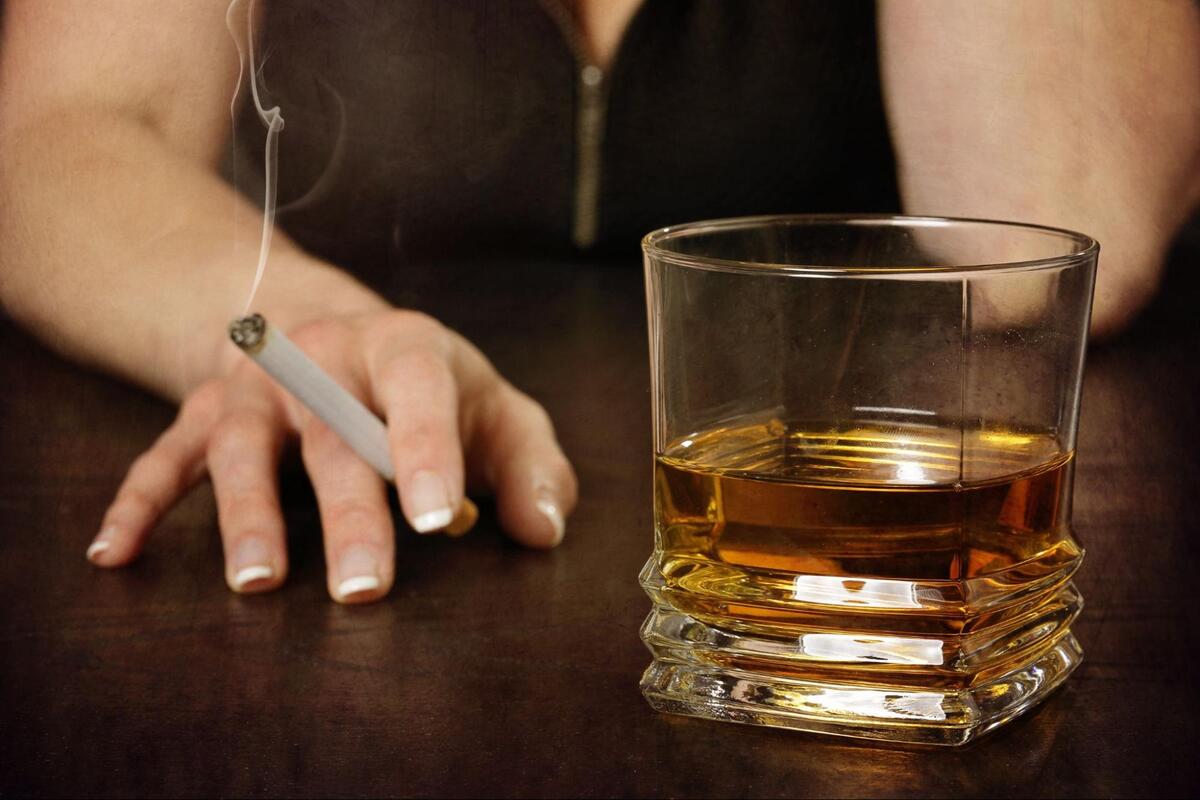お酒の入ったグラスとたばこを持つ手元